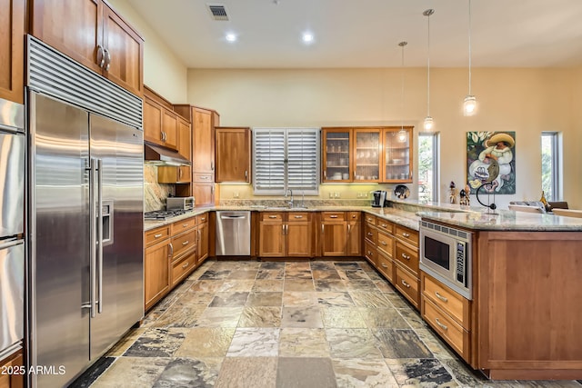 kitchen featuring pendant lighting, sink, built in appliances, kitchen peninsula, and light stone countertops