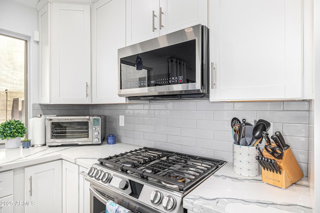 kitchen featuring appliances with stainless steel finishes, white cabinetry, backsplash, and light stone countertops