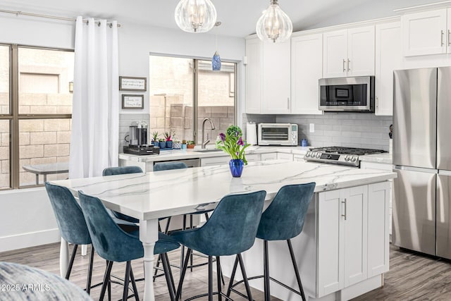 kitchen featuring appliances with stainless steel finishes, a sink, decorative backsplash, a breakfast bar area, and wood finished floors