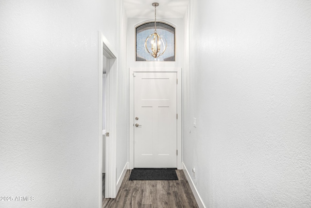 doorway featuring a chandelier, wood finished floors, baseboards, and a textured wall