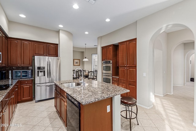 kitchen with a kitchen island with sink, dark stone counters, black appliances, pendant lighting, and sink