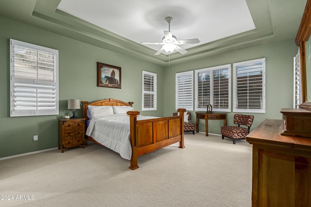 bedroom featuring light colored carpet, a raised ceiling, and ceiling fan