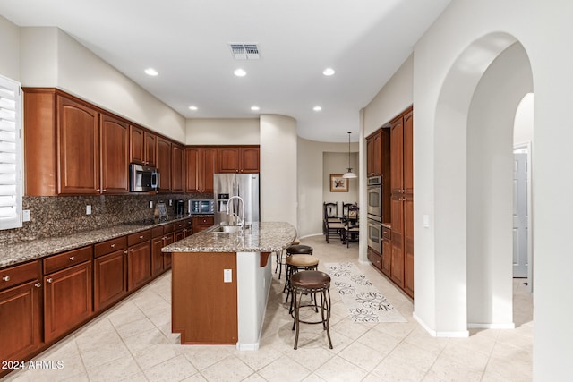 kitchen with appliances with stainless steel finishes, sink, dark stone counters, a breakfast bar, and a kitchen island with sink