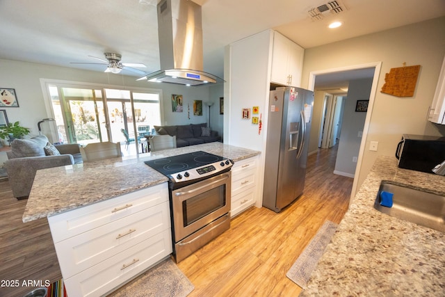 kitchen with light stone countertops, appliances with stainless steel finishes, island range hood, and white cabinets