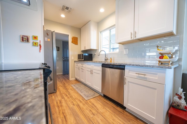 kitchen featuring light stone counters, light hardwood / wood-style flooring, white cabinets, stainless steel appliances, and backsplash