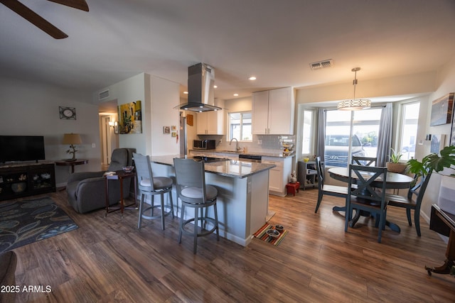 kitchen with sink, white cabinetry, island range hood, decorative light fixtures, and kitchen peninsula