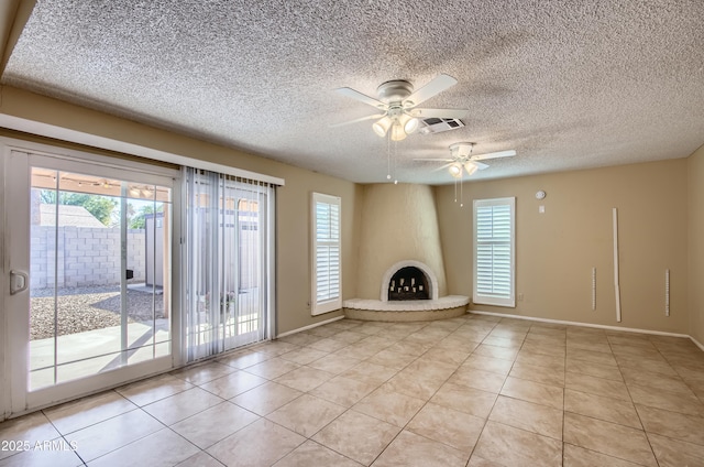 unfurnished living room with a fireplace, a textured ceiling, light tile patterned floors, and ceiling fan