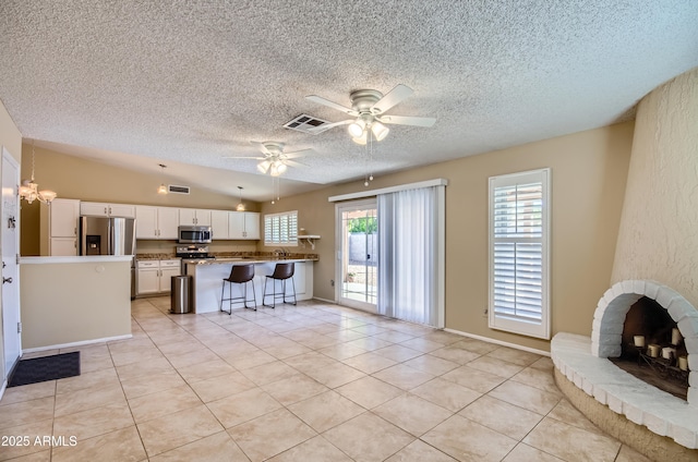 kitchen with appliances with stainless steel finishes, white cabinetry, a breakfast bar, vaulted ceiling, and light tile patterned flooring