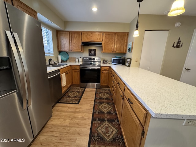 kitchen with light wood-style flooring, under cabinet range hood, stainless steel appliances, a peninsula, and brown cabinets