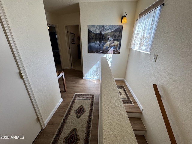 hallway with a textured wall, baseboards, and wood finished floors