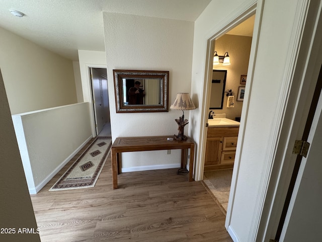 hallway featuring a sink, baseboards, and wood finished floors