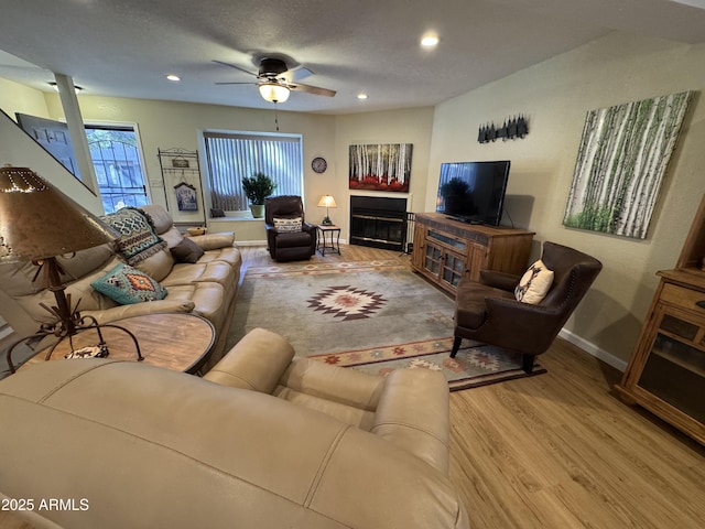 living area with baseboards, a glass covered fireplace, wood finished floors, and recessed lighting