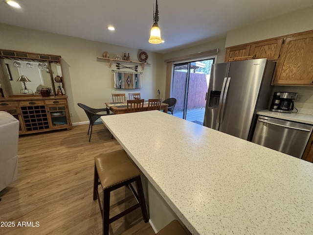 kitchen with light wood finished floors, appliances with stainless steel finishes, hanging light fixtures, light countertops, and a kitchen bar