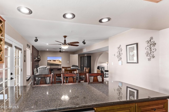 kitchen with a fireplace, ceiling fan, and dark stone countertops