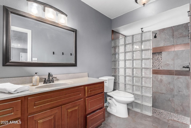 bathroom with a tile shower, vanity, and toilet