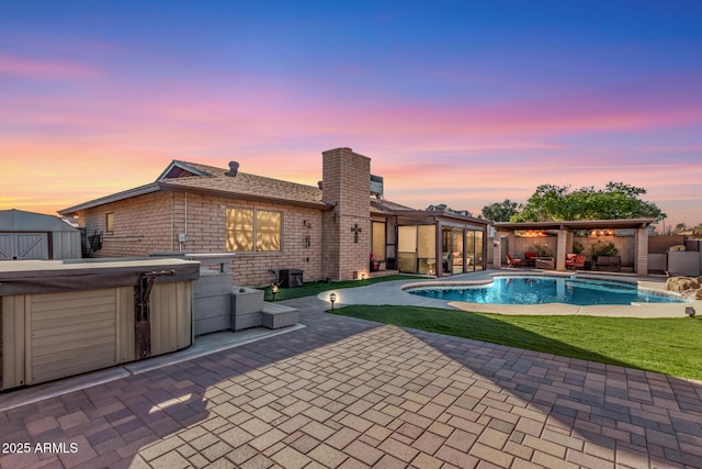 pool at dusk featuring a yard, a patio, a hot tub, and a shed