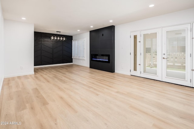 unfurnished living room featuring a tiled fireplace, french doors, and light hardwood / wood-style floors