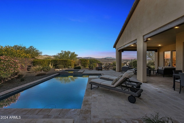 pool at dusk with a patio area, an in ground hot tub, outdoor lounge area, and a mountain view