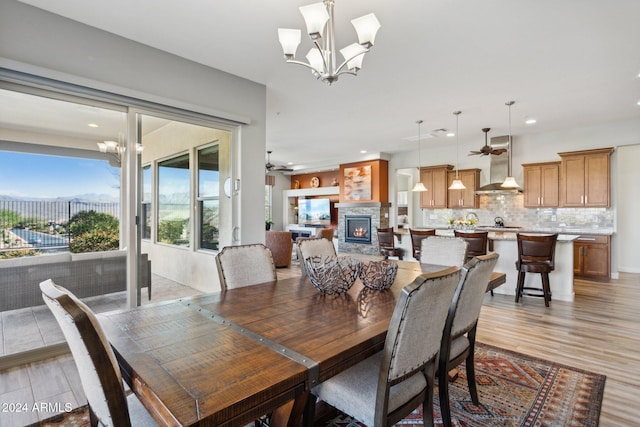 dining space featuring a fireplace, ceiling fan with notable chandelier, and light hardwood / wood-style floors