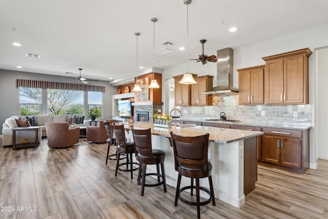 kitchen featuring wall chimney exhaust hood, a kitchen breakfast bar, light stone counters, decorative light fixtures, and stainless steel gas stovetop