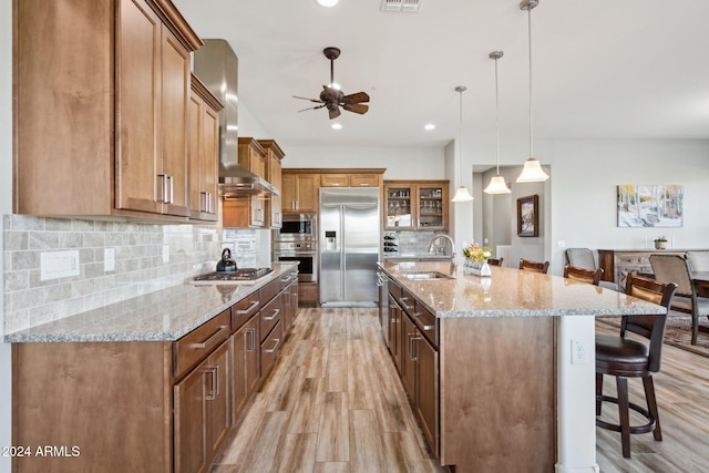 kitchen featuring a kitchen breakfast bar, a spacious island, hanging light fixtures, built in appliances, and wall chimney exhaust hood