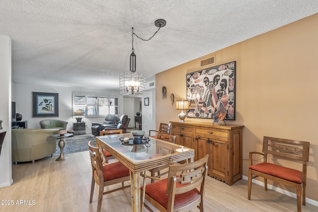 dining room with an inviting chandelier, light wood-type flooring, and a textured ceiling