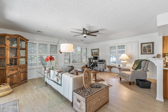 living room featuring ceiling fan, light wood-type flooring, and a textured ceiling