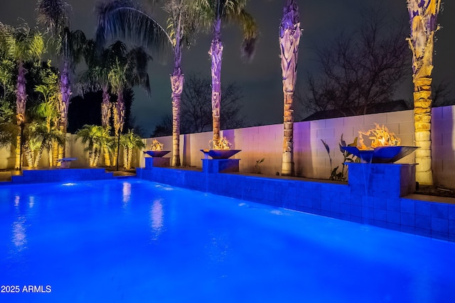 pool at night featuring pool water feature