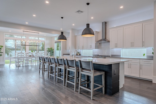 kitchen featuring pendant lighting, wall chimney exhaust hood, and a large island with sink