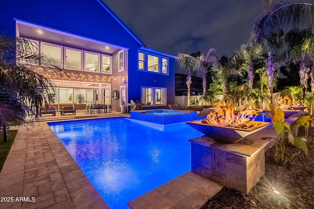 pool at night featuring an in ground hot tub, a patio, a fire pit, and french doors