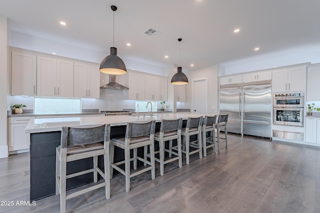 kitchen with appliances with stainless steel finishes, a large island, white cabinets, and wall chimney exhaust hood