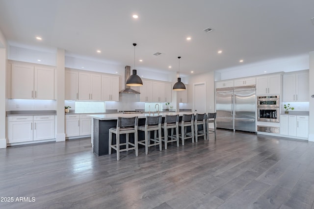 kitchen with white cabinetry, decorative light fixtures, ventilation hood, stainless steel appliances, and a kitchen island with sink