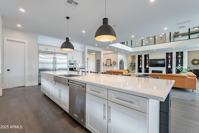 kitchen with sink, white cabinetry, appliances with stainless steel finishes, pendant lighting, and a kitchen island with sink