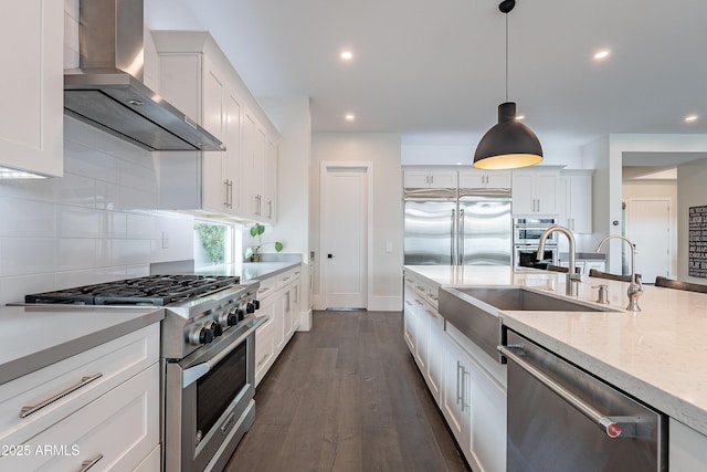 kitchen with wall chimney range hood, white cabinetry, hanging light fixtures, high quality appliances, and light stone countertops