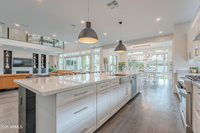 kitchen featuring sink, stainless steel appliances, a spacious island, white cabinets, and decorative light fixtures