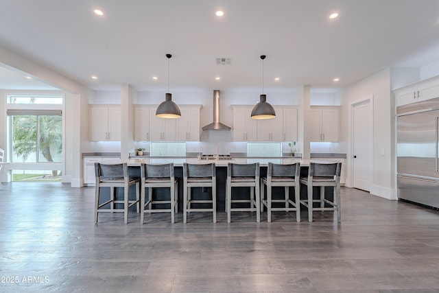 kitchen with pendant lighting, white cabinetry, a large island with sink, stainless steel built in fridge, and wall chimney range hood