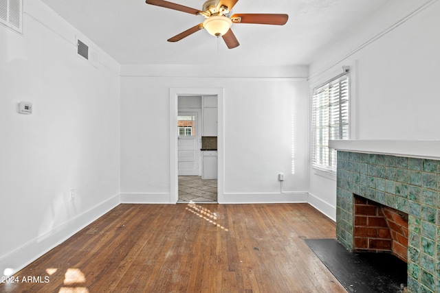 unfurnished living room featuring a tiled fireplace, ceiling fan, and wood-type flooring