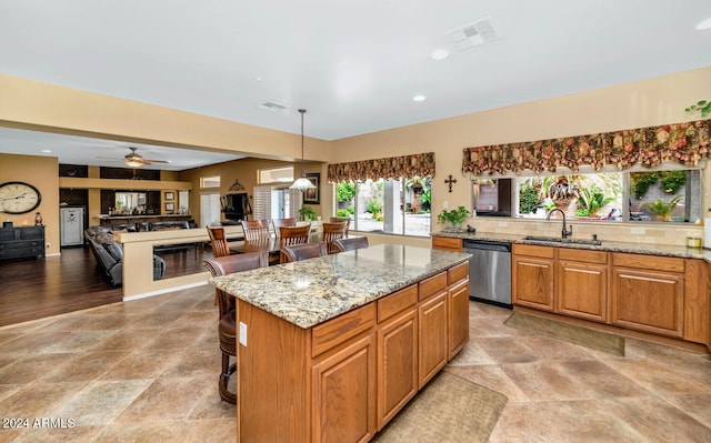 kitchen with light stone countertops, ceiling fan, a kitchen island, sink, and stainless steel dishwasher