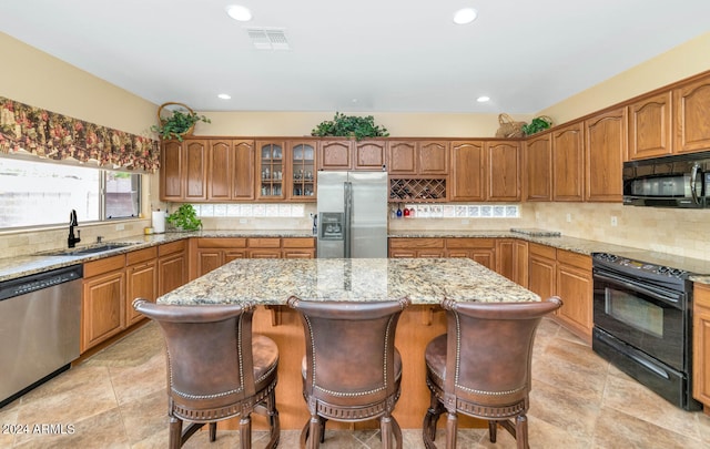 kitchen featuring light stone countertops, black appliances, a kitchen island, a breakfast bar area, and sink