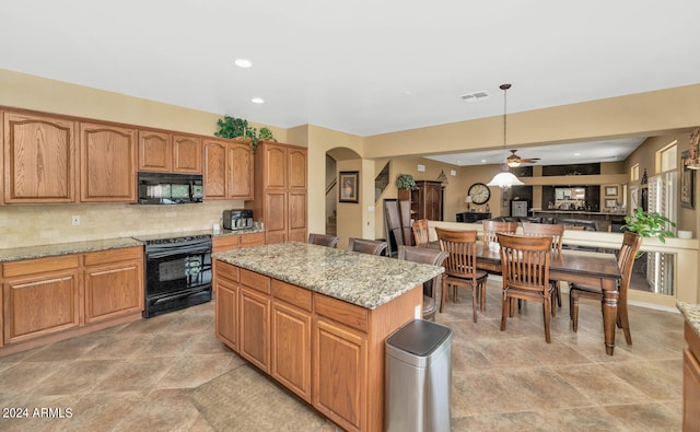 kitchen featuring light stone counters, black appliances, decorative backsplash, a kitchen island, and ceiling fan