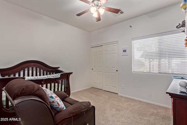 carpeted bedroom with a closet, ceiling fan, and a crib