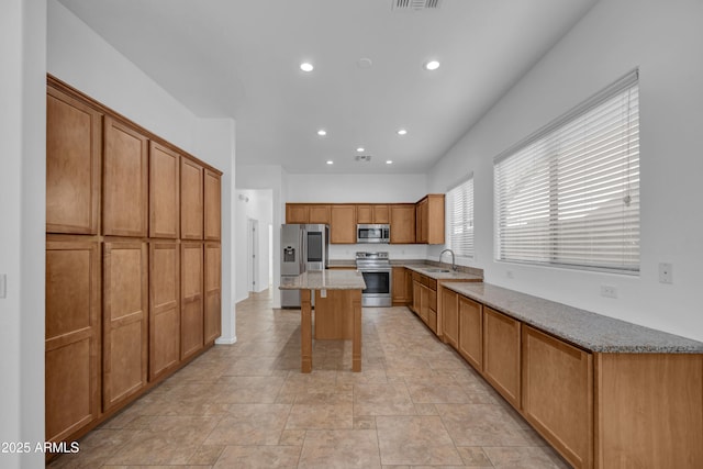 kitchen with sink, a kitchen breakfast bar, a center island, stainless steel appliances, and light stone countertops