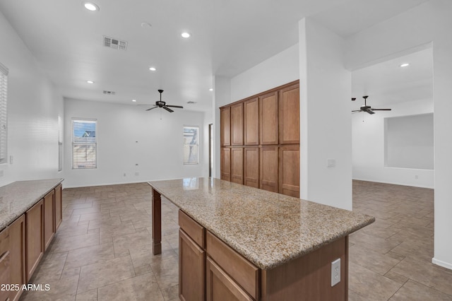 kitchen with light stone counters, ceiling fan, and a kitchen island