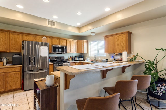 kitchen with stainless steel appliances, a breakfast bar, a peninsula, a sink, and light countertops