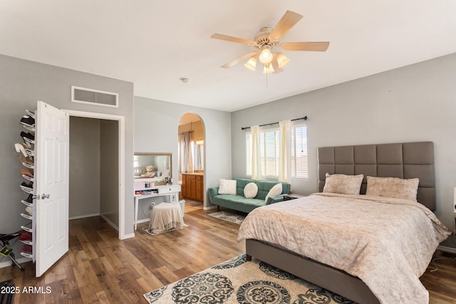 bedroom with arched walkways, ceiling fan, wood finished floors, visible vents, and baseboards