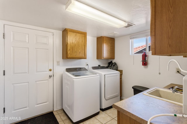 clothes washing area featuring light tile patterned flooring, a sink, visible vents, cabinet space, and washing machine and clothes dryer