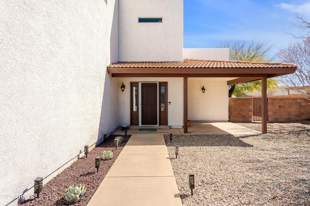 entrance to property featuring a tiled roof, fence, and stucco siding