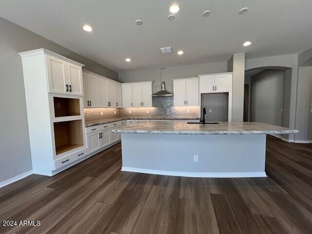 kitchen with light stone countertops, white cabinetry, and a kitchen island with sink