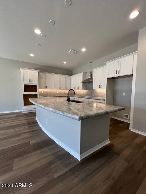 kitchen featuring light stone counters, a center island with sink, white cabinetry, and sink