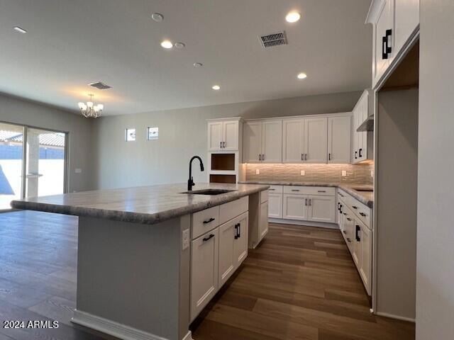 kitchen featuring sink, light stone countertops, an island with sink, white cabinetry, and a chandelier